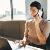 Smiling woman with smartphone in hand. She uses onOffice enterprise on her laptop.