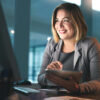Femme devant un ordinateur de bureau avec une tablette à la main