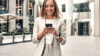 Frau in der Stadt die am Smartphone nach Immobilien Trends sucht