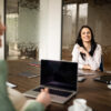 Zwei Frauen sitzen mit Laptop und Tablet an einem Meetingtisch